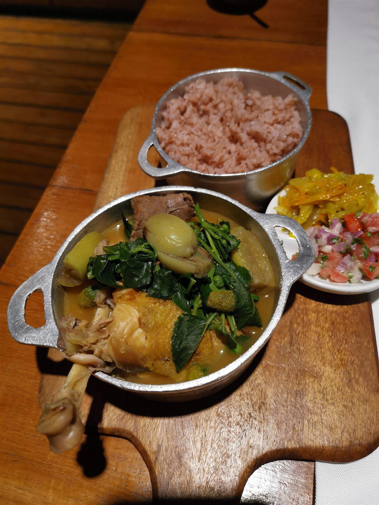 Romazava servi en cocotte, avec riz, achards et salade de tomates — un repas malgache complet.